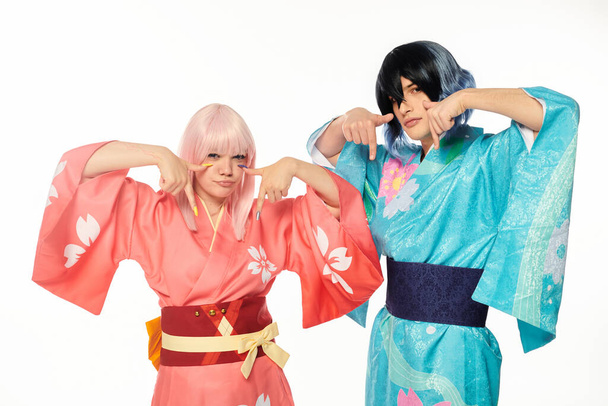 молодые косплееры в ярких кимоно, показывающих вниз пальцами на белом, аниме-стиле - Фото, изображение