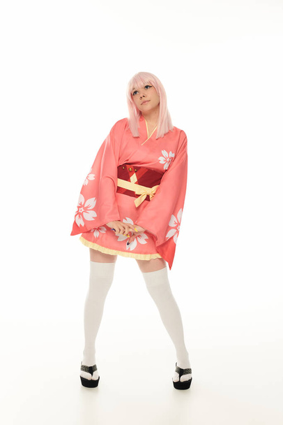affascinante donna cosplay bionda in kimono rosa e parrucca bionda in piedi su bianco, lunghezza intera - Foto, immagini