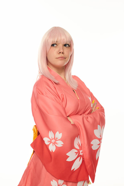 вдумчивая блондинка в розовом кимоно со сложенными руками, смотрящая на белую косплейную моду - Фото, изображение