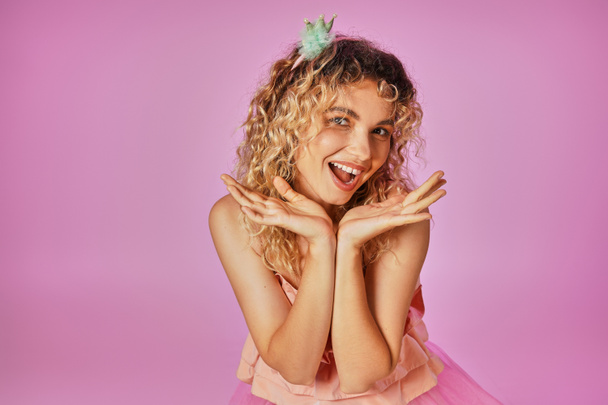 cheerful attractive woman in pink costume of tooth fairy smiling at camera with hands close to face - Photo, Image