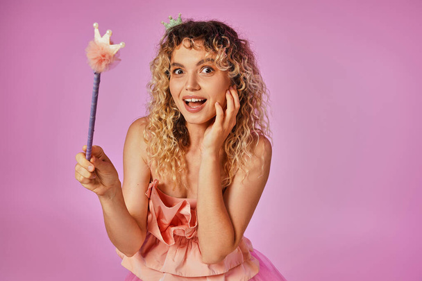 užaslá veselá blondýna žena v růžovém kostýmu zubní víly drží kouzelnou hůlku a dívá se do kamery - Fotografie, Obrázek