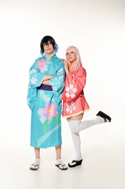 mujer apoyada en novio en colorido kimono y peluca de pie con los brazos cruzados en blanco, cosplay - Foto, imagen