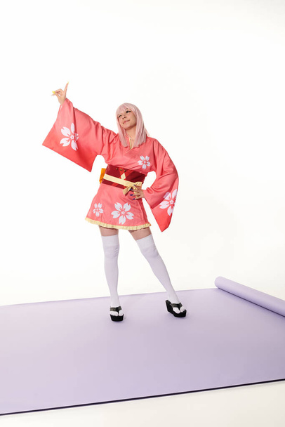 expresivní anime styl žena v růžovém kimonu s rukou na boku ukazuje nahoru s prstem na bílé - Fotografie, Obrázek