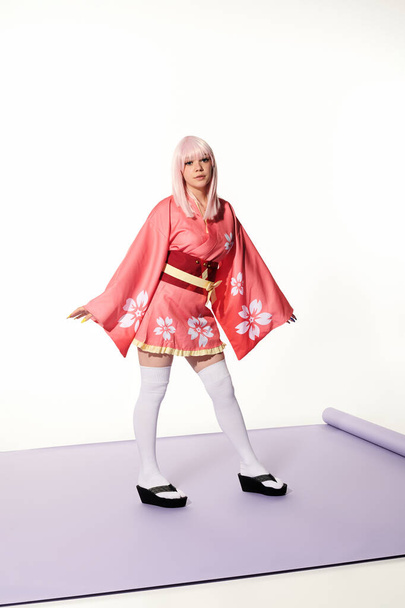 japanese cosplay subculture, blonde woman in kimono and wig on purple carper and white backdrop - Photo, Image