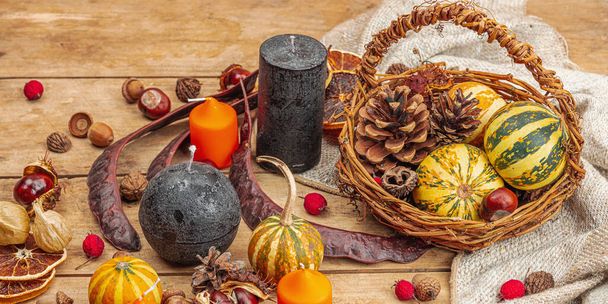 Autumn cozy composition. Pumpkins in a basket, candles, cones, seeds. Traditional fall decor, seasonal good mood. Flat lay, wooden background, banner format - Photo, Image