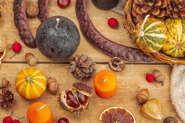 Autumn cozy composition. Pumpkins in a basket, candles, cones, seeds. Traditional fall decor, seasonal good mood. Flat lay, wooden background, top view - Photo, Image