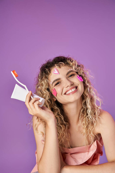 portrait de femme joyeuse avec brosse à dents et pâte dans les mains souriantes et posant sur fond rose - Photo, image