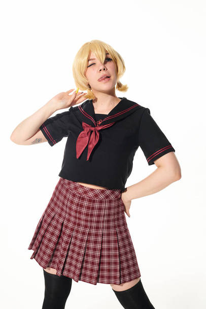 verleidelijke anime stijl vrouw in geel blond pruik en school uniform poseren met de hand op heup op wit - Foto, afbeelding