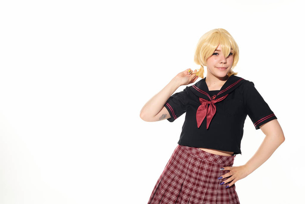 glimlachende anime stijl vrouw in school uniform vasthouden hand op heup en kijken naar camera op wit - Foto, afbeelding