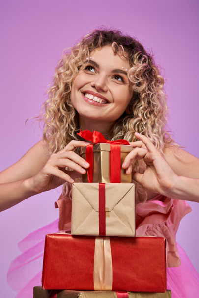portrait of dreamy pretty woman with curly hair touching pile of gifts with fingers and looking away - Photo, Image