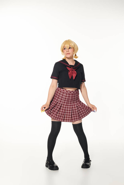 cosplay subkultura, mladá žena v paruce a školní uniformě s kostkovanou sukní na bílém pozadí - Fotografie, Obrázek