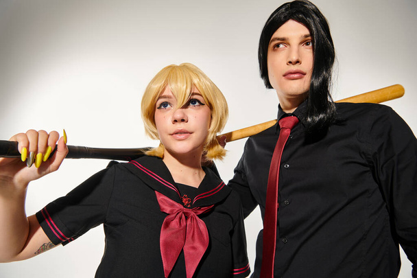 couple of cosplayers in wigs and school uniform with baseball bats looking away on grey, subculture - Photo, Image