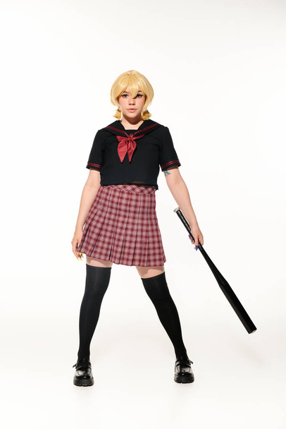 pleine longueur de cosplayer féminin confiant en uniforme scolaire posant avec batte de baseball sur blanc - Photo, image