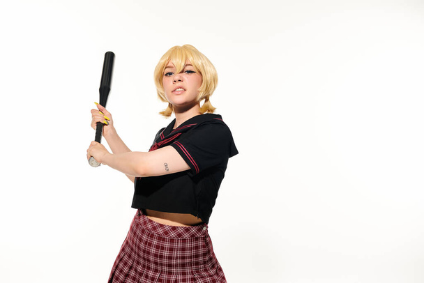 geïrriteerde vrouw in school uniform en pruik staan met honkbalknuppel op wit, cosplay karakter - Foto, afbeelding