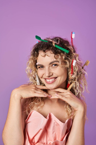 mujer alegre en vestido rosa y cepillos de dientes en su cabello, manos debajo de su barbilla, concepto de hada de los dientes - Foto, Imagen