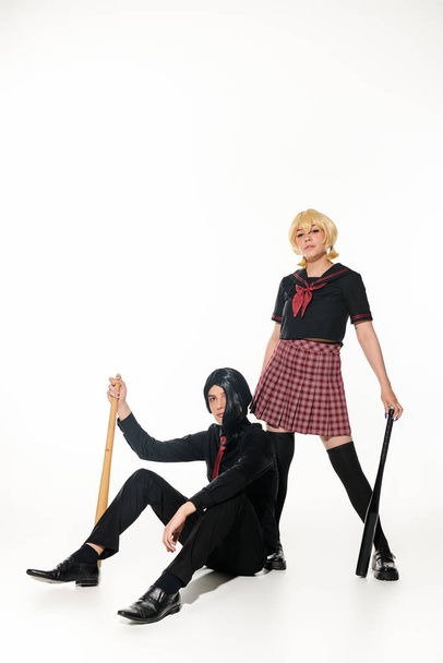 jistý anime styl pár ve školní uniformě a paruky s pózováním s baseballovými pálkami na bílém - Fotografie, Obrázek