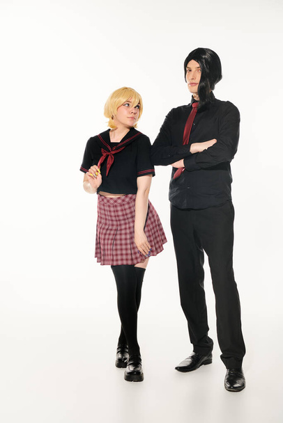 femme en perruque blonde regardant l'homme en vêtements noirs avec les bras croisés sur blanc, étudiants de style anime - Photo, image