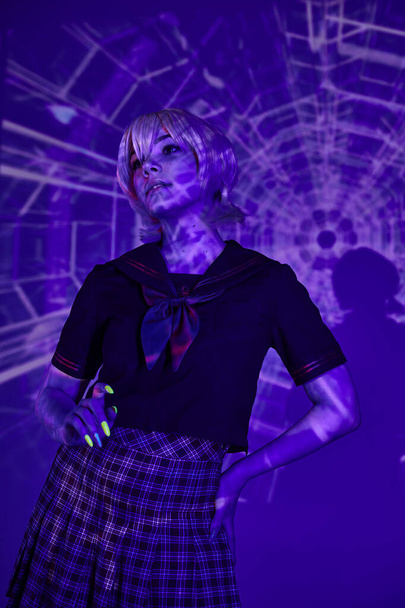 mladá anime styl žena ve školní uniformě pózování s rukou na boku v modré abstraktní projekce - Fotografie, Obrázek