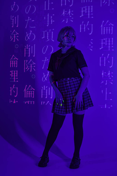 jovem mulher em uniforme escolar em luz de néon azul com projeção de hieróglifos, conceito de cosplay - Foto, Imagem