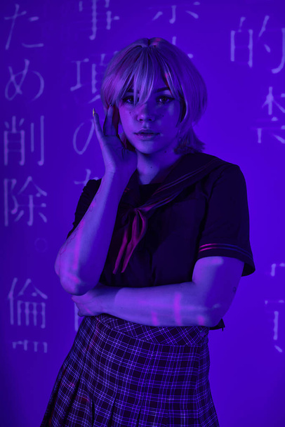 mulher em peruca loira e uniforme escolar em luz de néon azul com projeção de hieróglifos, tendência de anime - Foto, Imagem