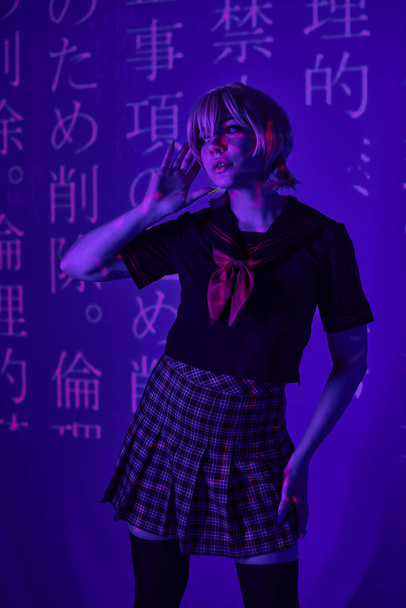 jonge vrouw in schooluniform kijken weg in blauw neon licht met hiërogliefen projectie, cosplay - Foto, afbeelding