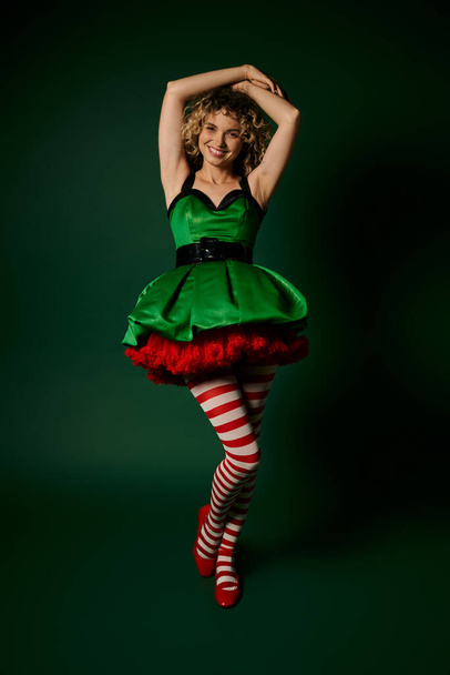 mulher alegre vestida como elfo do ano novo posando com o braço levantado para o cabelo e sorrindo para a câmera - Foto, Imagem