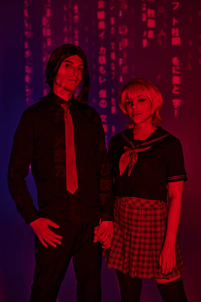 anime style students in uniform holding hands in red neon light on abstract purple backdrop - Photo, Image
