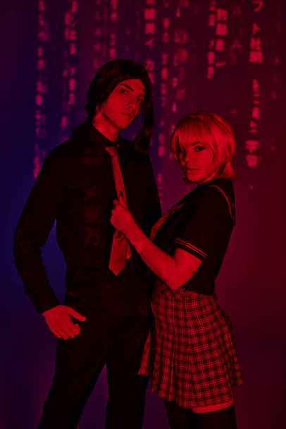 аниме пара в студентах, смотрящих на камеру в красном неоновом свете на абстрактном фиолетовом фоне - Фото, изображение