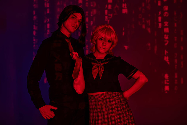 anime žena ve studentských uniformách tahání kravatu muže v červeném neonovém světle na fialové abstraktní pozadí - Fotografie, Obrázek