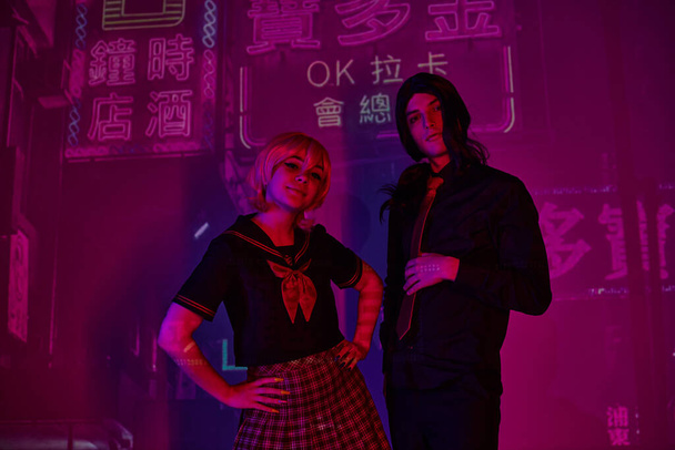 anime vrouw met handen op heupen in de buurt trendy man in neon licht op paarse achtergrond met hiërogliefen - Foto, afbeelding