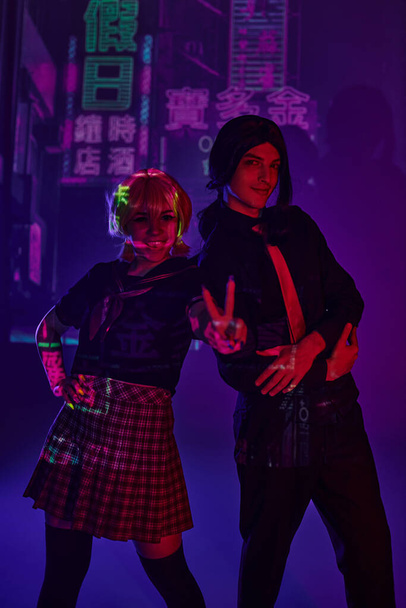 anime woman in school uniform showing victory sign near man on purple neon backdrop with hieroglyphs - Photo, Image
