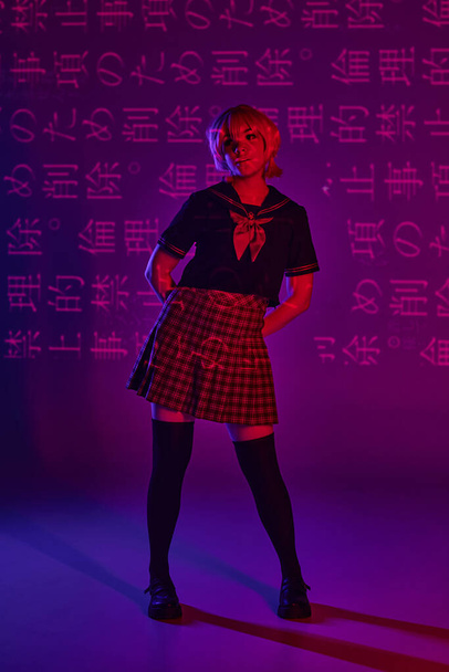 mujer joven posando en uniforme escolar sobre fondo púrpura neón con jeroglíficos, estilo anime - Foto, Imagen
