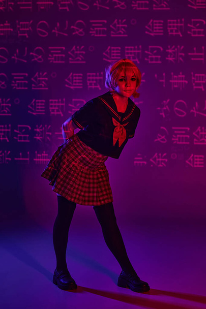 csinos nő iskolai egyenruhában pózol neon lila háttér hieroglifák, anime trend - Fotó, kép