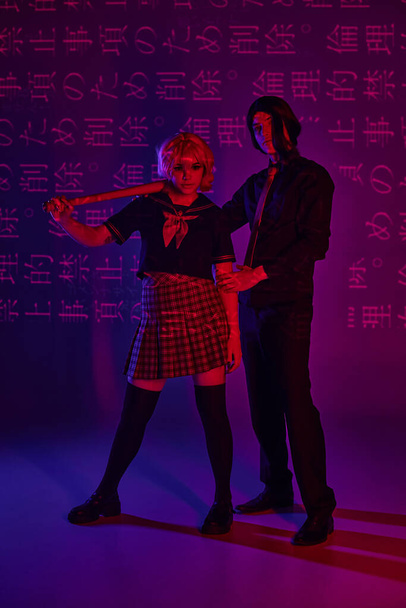 anime žena s baseballovou pálkou v blízkosti muže v paruce na neonově fialové pozadí s hieroglyfy projekce - Fotografie, Obrázek