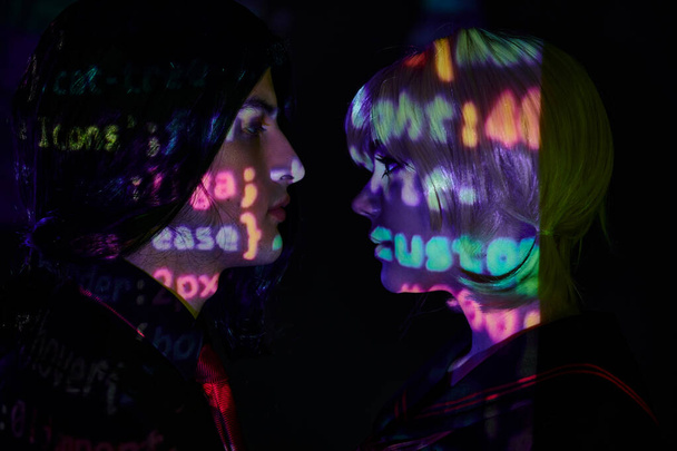 vista lateral de los jóvenes estudiantes con letras de programación de neón sobre fondo oscuro, concepto de tendencia de anime - Foto, Imagen