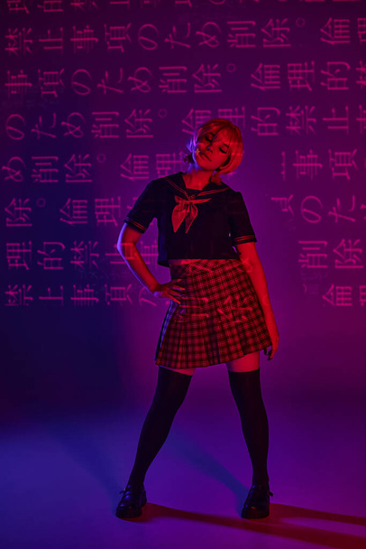 anime woman in school uniform with hand on hip in neon light on purple backdrop with hieroglyphs - Photo, Image