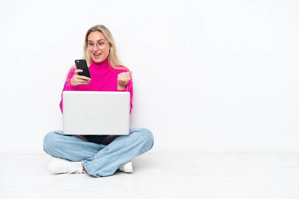 Молода біла жінка з ноутбуком сидить на підлозі здивована і відсилає повідомлення
 - Фото, зображення