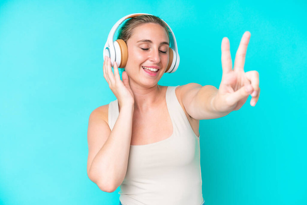 Nuori valkoihoinen nainen eristetty sinisellä taustalla kuuntelee musiikkia ja laulaa - Valokuva, kuva