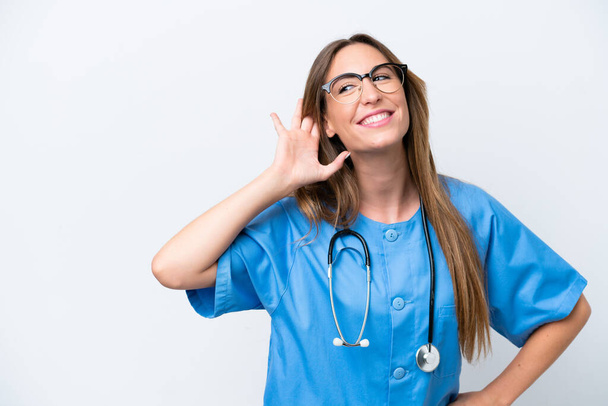 Nuori kirurgi lääkäri nainen eristetty sinisellä taustalla kuuntelemalla jotain laittamalla käsi korvaan - Valokuva, kuva