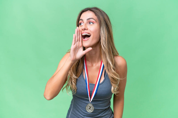 Giovane bella donna uruguaiana sport con medaglie su sfondo isolato gridando con la bocca spalancata al laterale - Foto, immagini