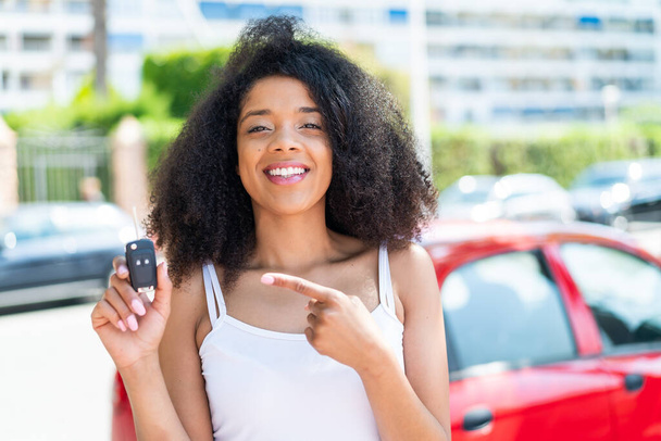 Young African American woman holding car keys at outdoors and pointing it - Photo, Image