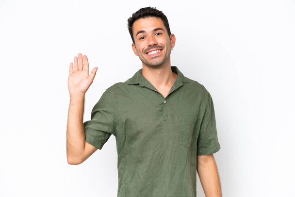 Joven hombre guapo sobre fondo blanco aislado saludando con la mano con expresión feliz
 - Foto, Imagen