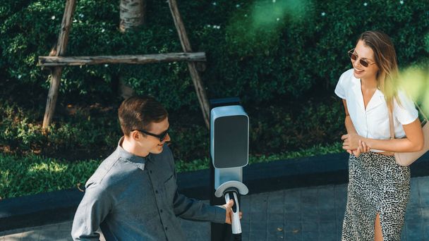Jóvenes viajan en pareja con el coche eléctrico EV cargando en verde ciudad sostenible jardín al aire libre en verano muestra estilo de vida de sostenibilidad urbana por verde limpia energía recargable de vehículos eléctricos innards - Foto, imagen