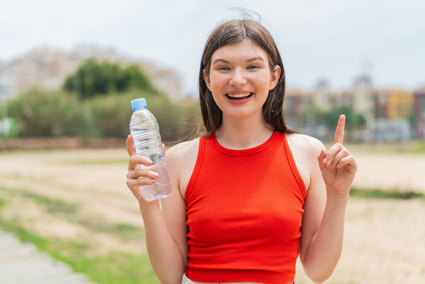 Молодая красивая украинка с бутылкой воды на открытом воздухе указывает на отличную идею - Фото, изображение