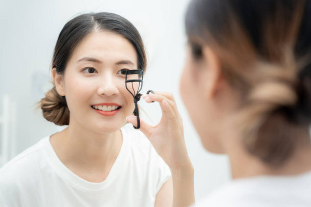 Kaunis aasialainen nainen istuu peilin edessä hymy ja curling silmäripset. kasvot terve nainen soveltamalla meikkiä. Mainos, elämäntapa, kosmetiikka, tarvikkeet, kauneusaktiviteetti, kosmetologi - Valokuva, kuva