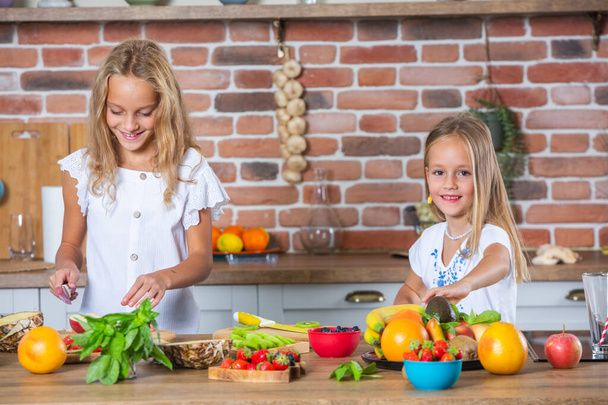 Δύο κοριτσάκια στην κουζίνα με φρέσκα λαχανικά. Υγιεινή διατροφή. Χαρούμενες αδερφές. - Φωτογραφία, εικόνα
