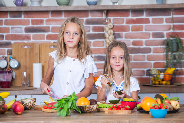 Twee kleine meisjes in de keuken met verse groenten. Gezond voedsel concept. Gelukkige zussen. - Foto, afbeelding