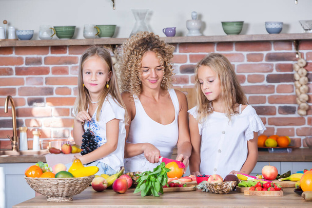 Mother and daughters cooking together in the kitchen. Healthy food concept. Portrait of happy family with fresh smoothies. - Photo, Image
