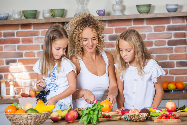 キッチンで一緒に料理をする母と娘たち. 健康食品のコンセプト。 新鮮なスムージーと幸せな家族の肖像画. - 写真・画像