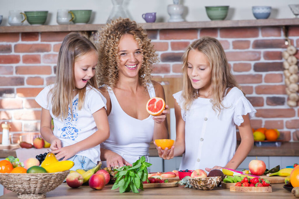 Mother and daughters cooking together in the kitchen. Healthy food concept. Portrait of happy family with fresh smoothies. - Photo, Image